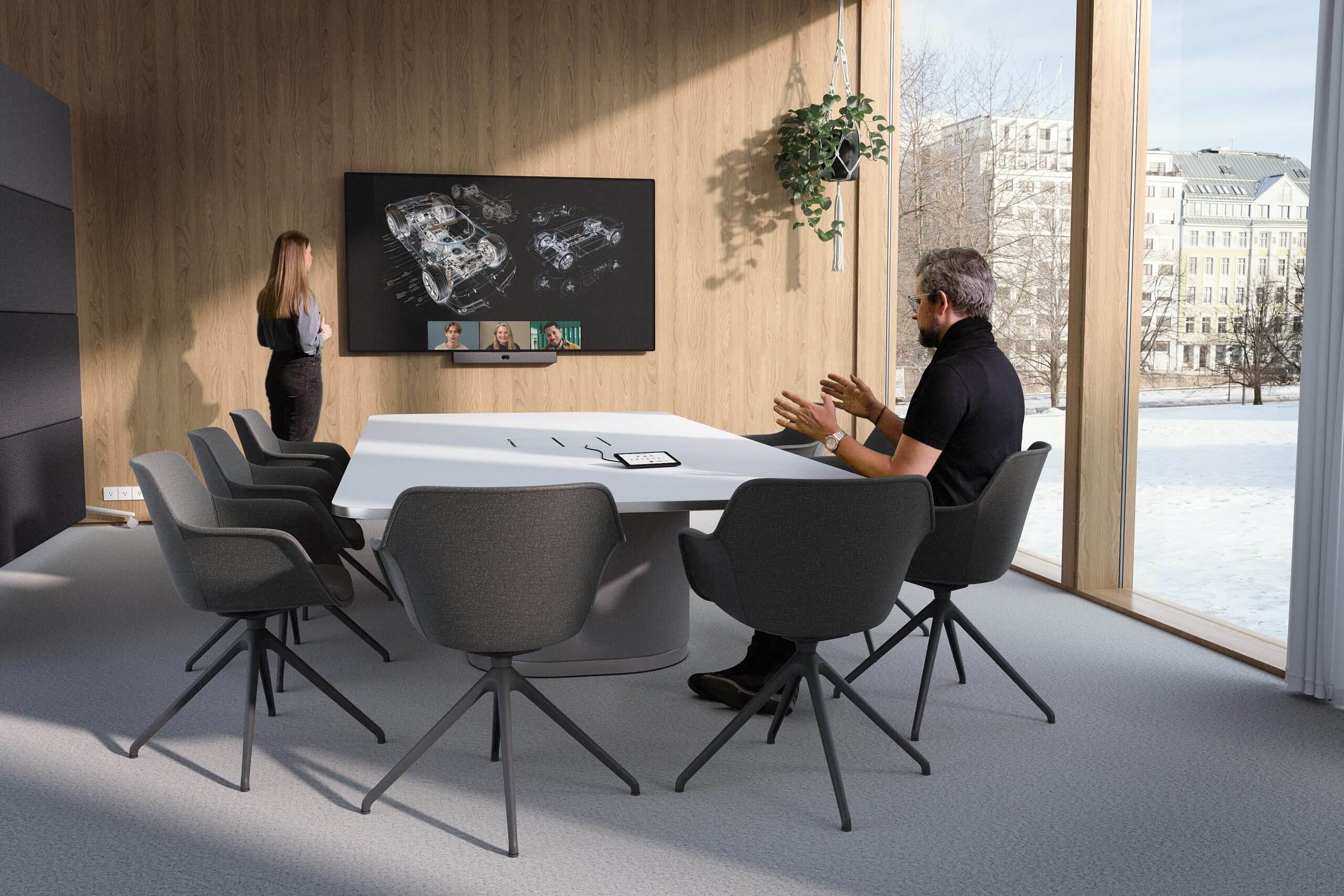 Conference room with two people at a table with 6 chairs, and tv on wall.